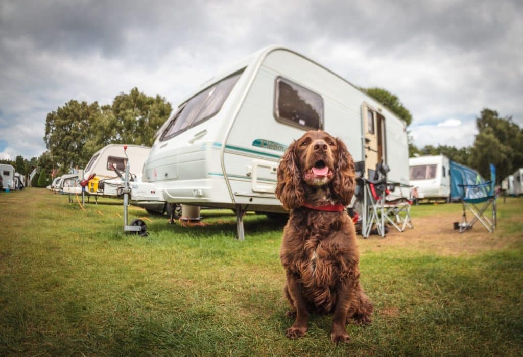 Family relaxing outside their caravan camper with chairs and campfire, emphasizing the leisure aspect