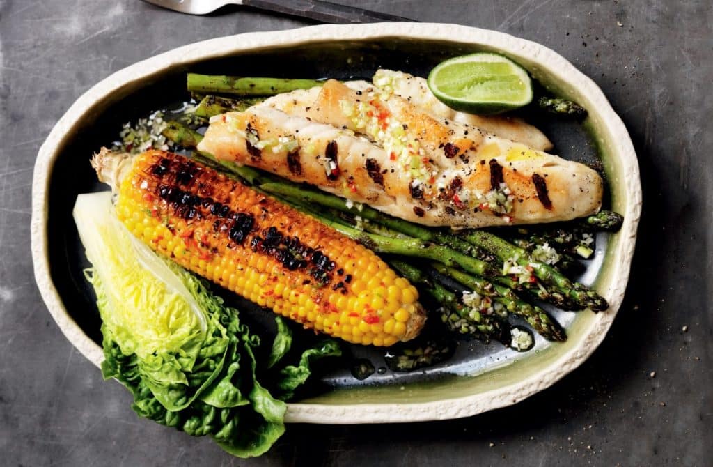 Colorful platter of grilled fish with various sides, emphasizing a complete meal