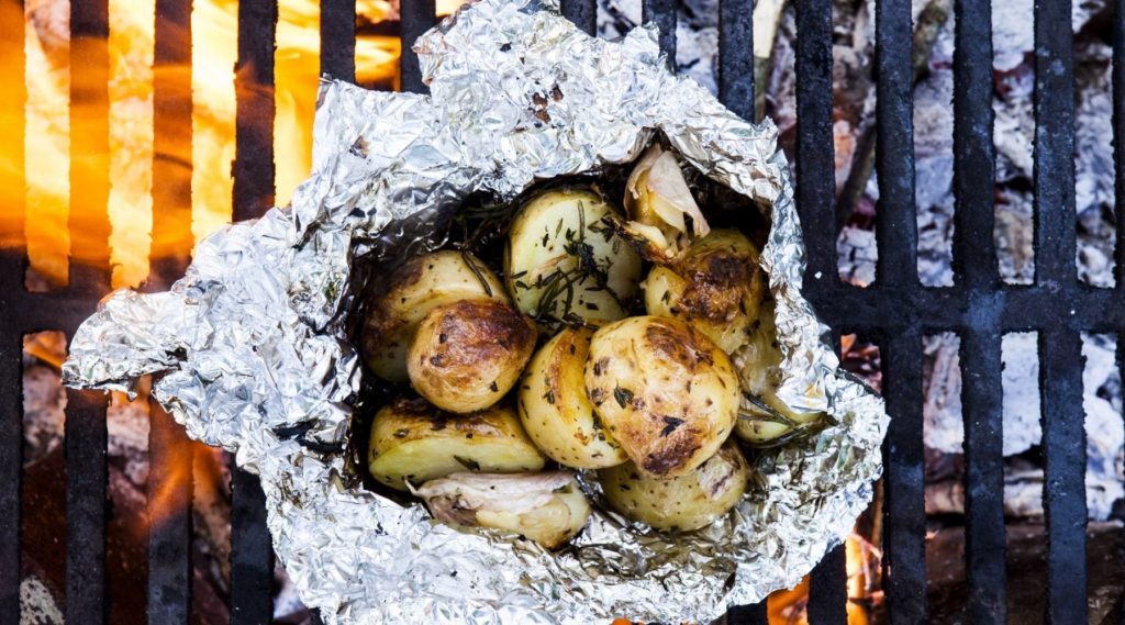 Foil-wrapped potatoes cooked in campfire embers,