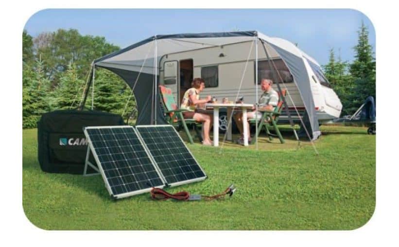 A portable solar panel rests on the ground, powering a caravan parked outdoors