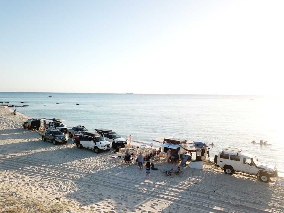 Retro caravans with an awning open, parked on a golden sand beach with gentle waves lapping at the shore