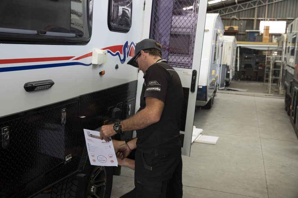 Caravan technician inspects the exterior of a motorhome inside a workshop