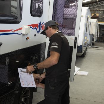 Caravan technician inspects the exterior of a motorhome inside a workshop