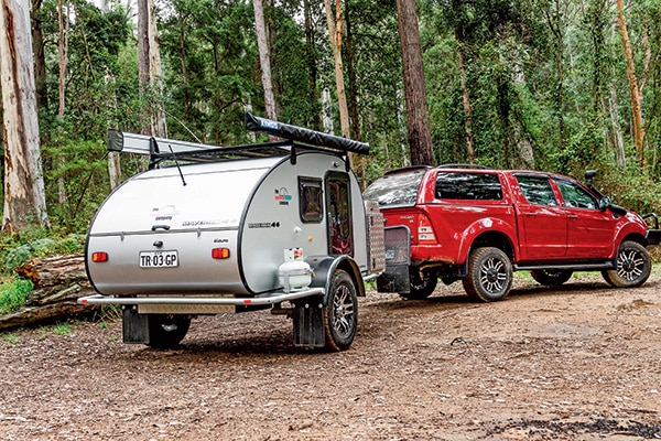 Tiny teardrop camper trailer towed by a truck on a scenic route