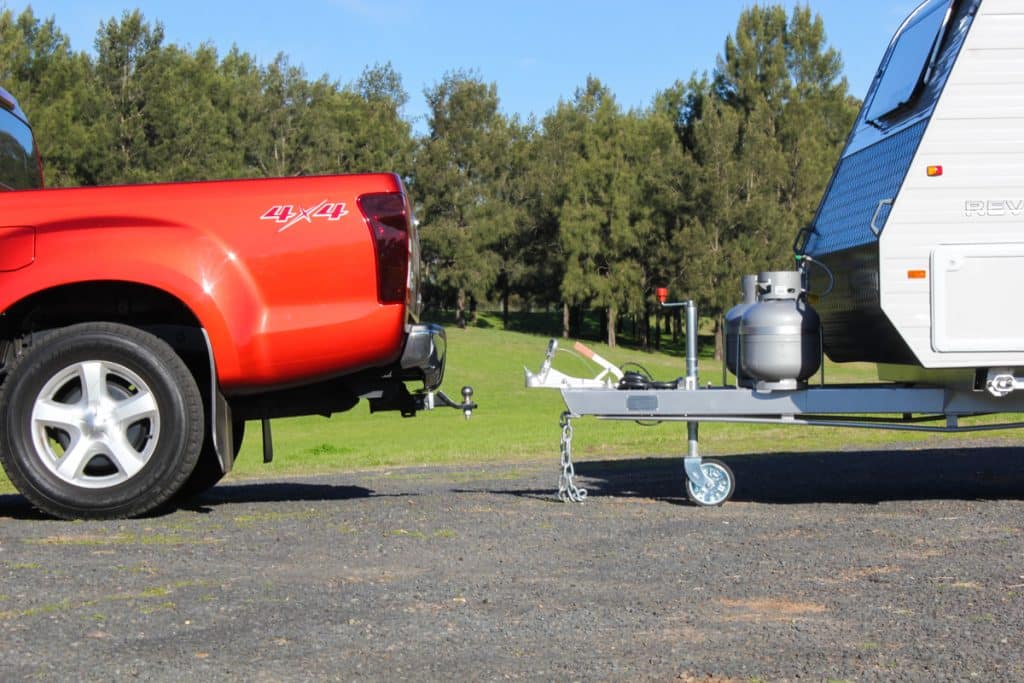 Caravan secured on a truck bed, using a jockey wheel for additional stability during the loading and unloading process