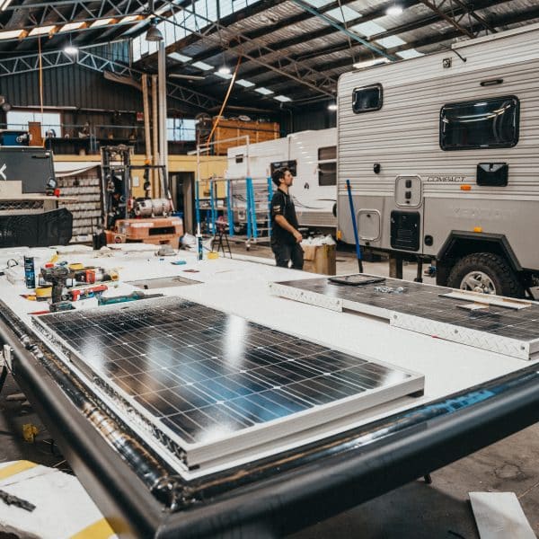 Keeping your caravan energy efficient: Two technicians service and reattach a solar panel for continued power