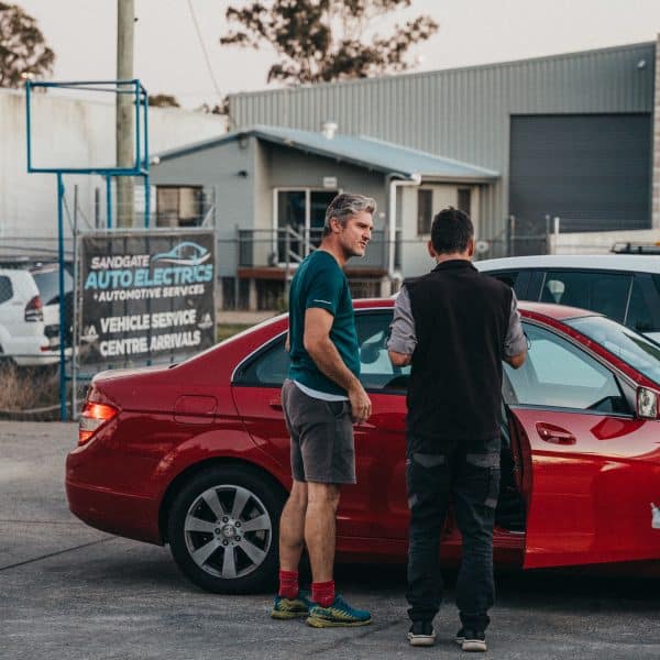 Two people discuss pre-purchase or safety checks in front of a red vehicle