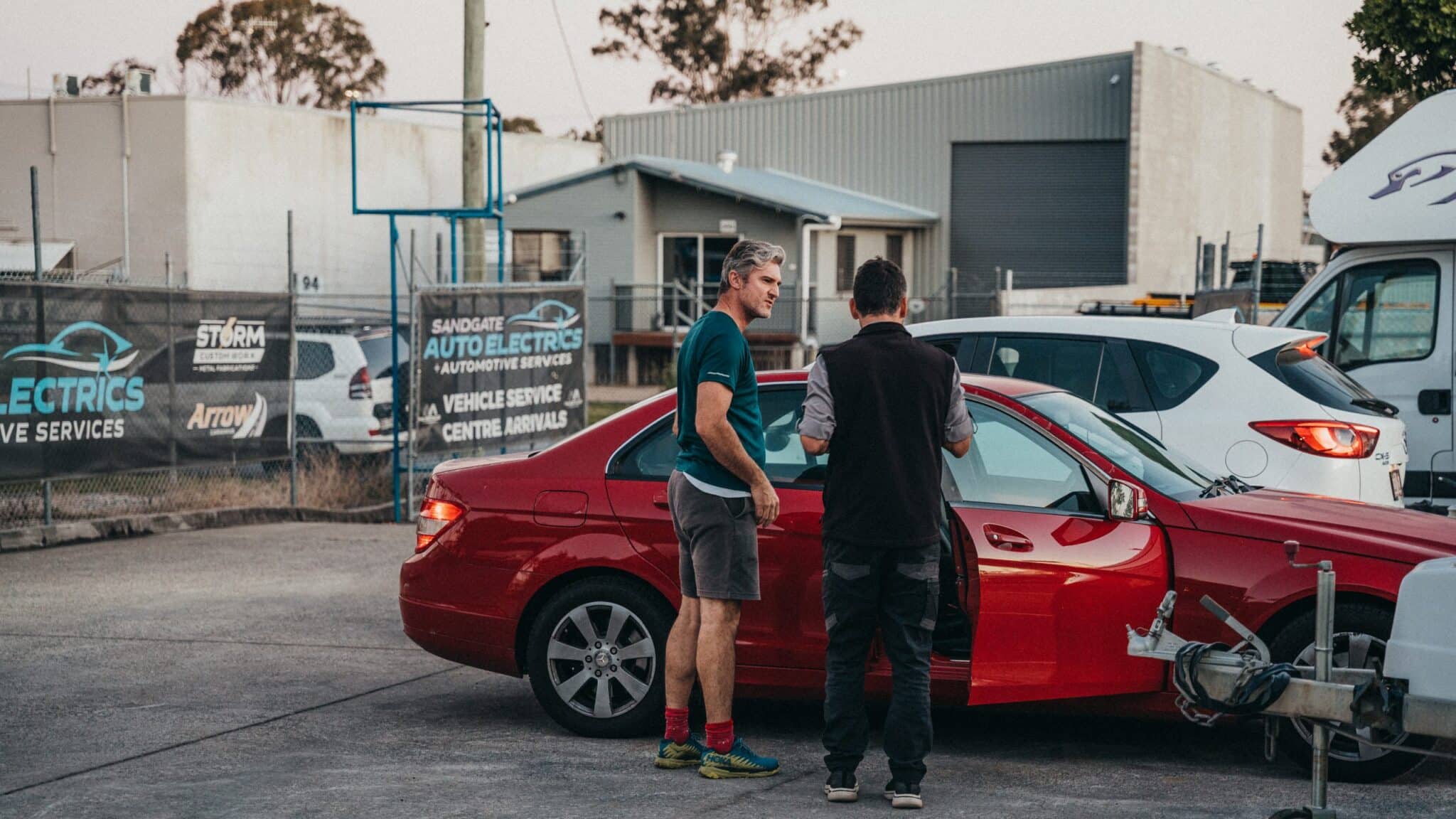 Two people discuss pre-purchase or safety checks in front of a red vehicle
