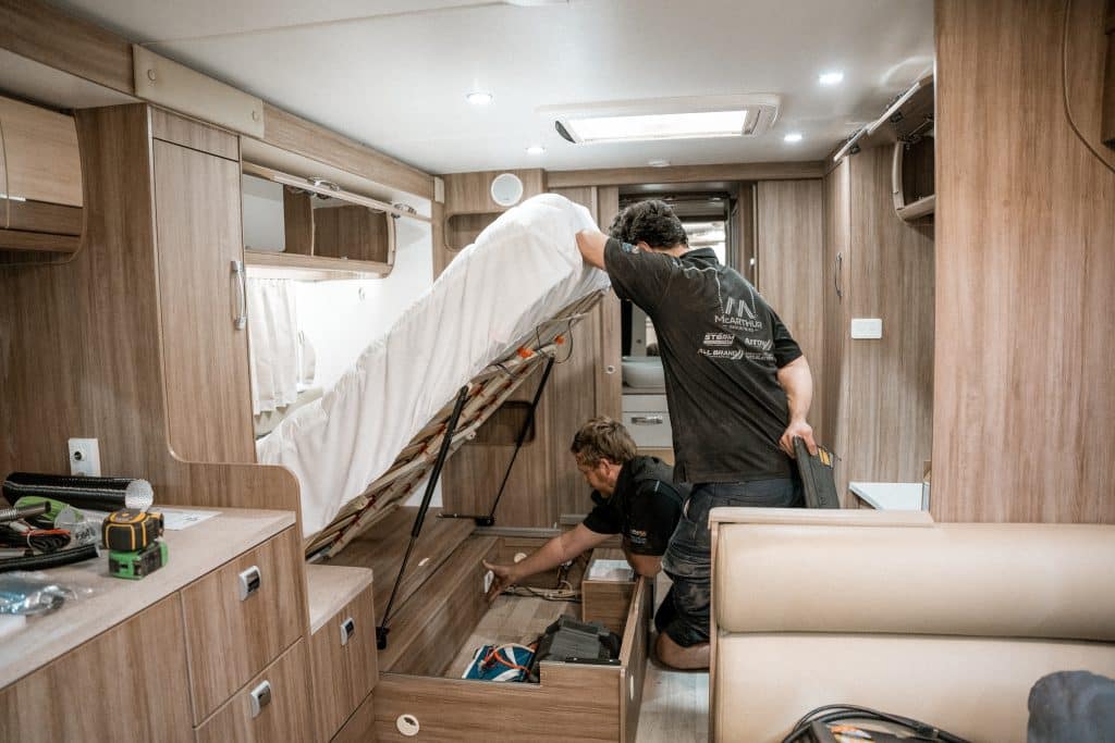 Two technicians working on a caravan inside a workshop