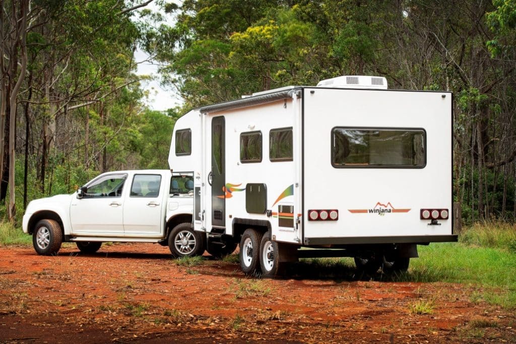 Pickup truck with a camper shell parked beside a small white camper trailer with a pop-up top, at a campsite in a wooded area