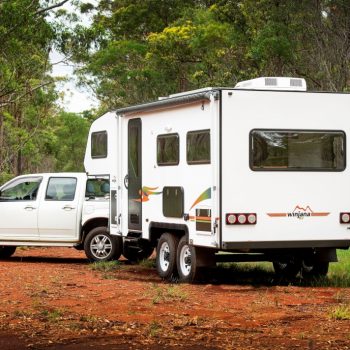 Pickup truck with a camper shell parked beside a small white camper trailer with a pop-up top, at a campsite in a wooded area