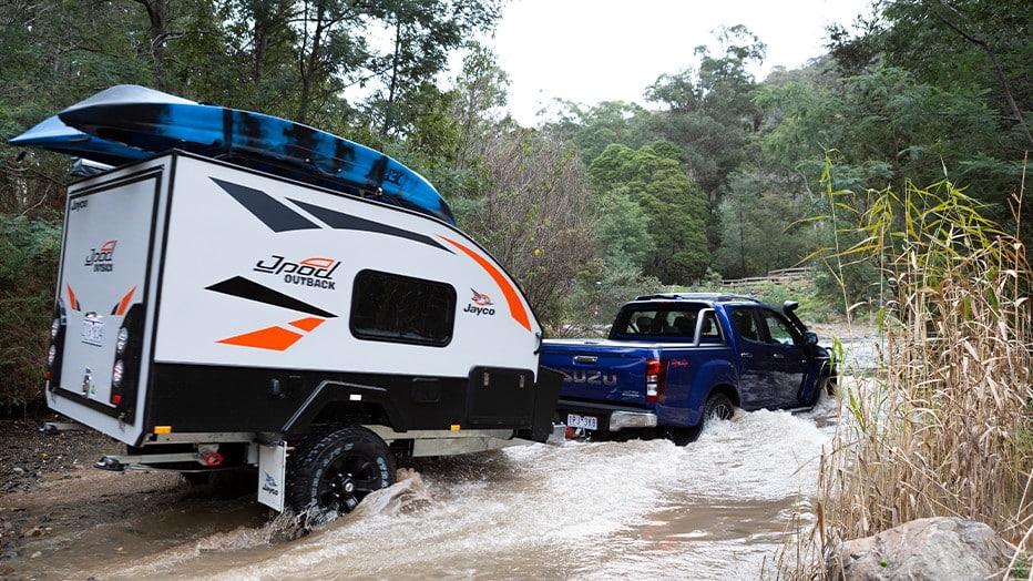 Blue truck pulls a pod camper across a river