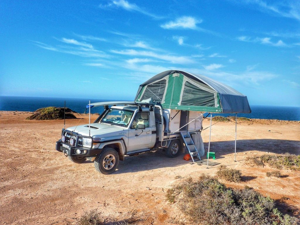 Pickup truck and camper trailer set up for camping in a scenic location with trees and a dirt road