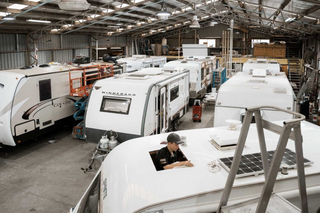 Technician inspecting and repairing the roof of a parked caravan inside a workshop