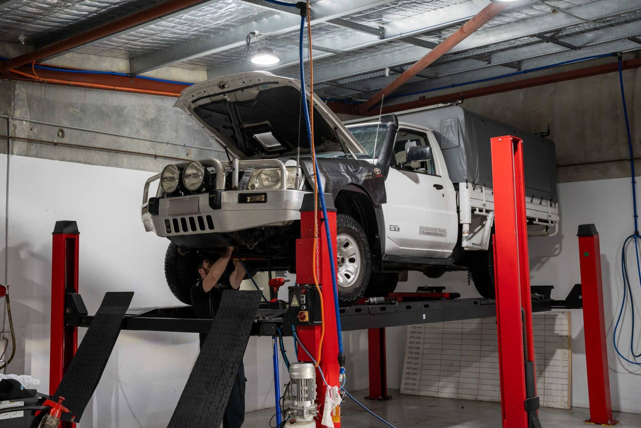 A technician in Brisbane upgrades a vehicle's Automatic Teller Machine system, working under the open hood of an elevated car