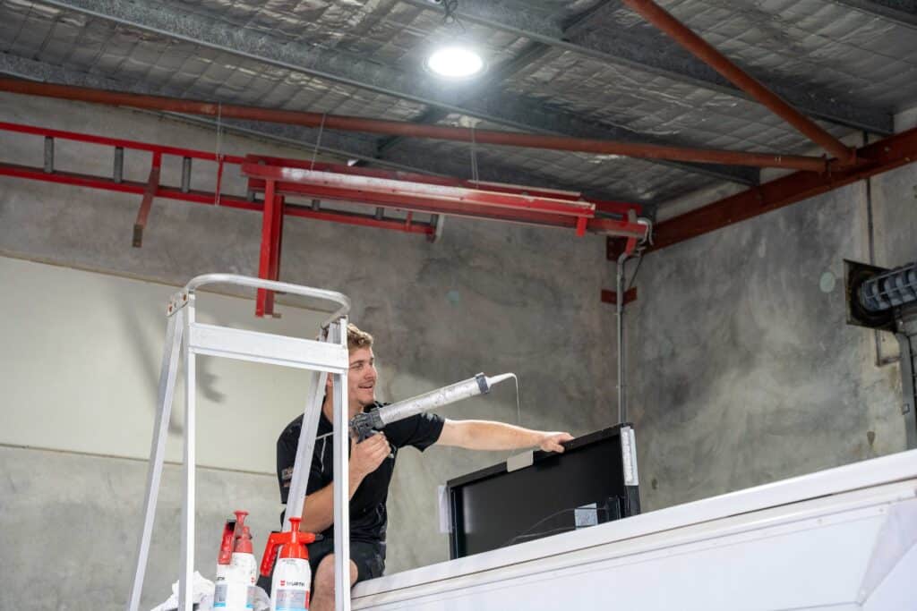 technician uses specialized tools to patch a tear in a caravan roof inside a brightly lit workshop