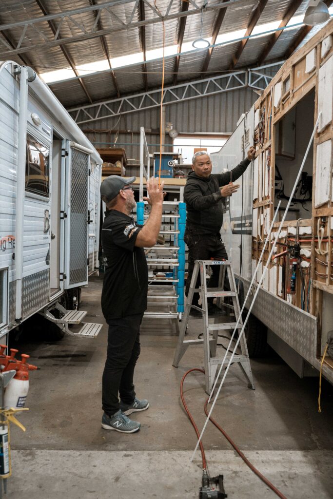 Technician resealing caravan windows with new sealant inside a workshop