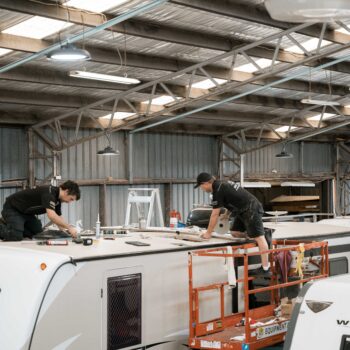 Technicians collaboratively repair a caravan roof inside a workshop