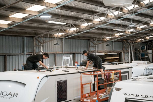 Technicians collaboratively repair a caravan roof inside a workshop