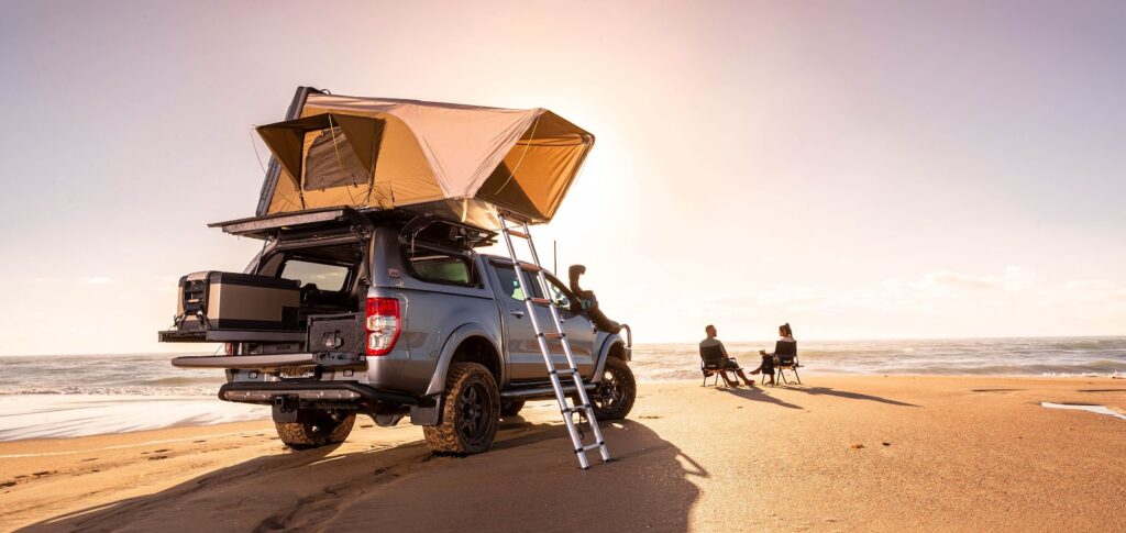 Pickup truck and pop-up camper trailer parked at a scenic campsite with beach access