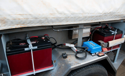 Two black 2V batteries secured beneath a caravan, providing additional power storage for off-grid use.