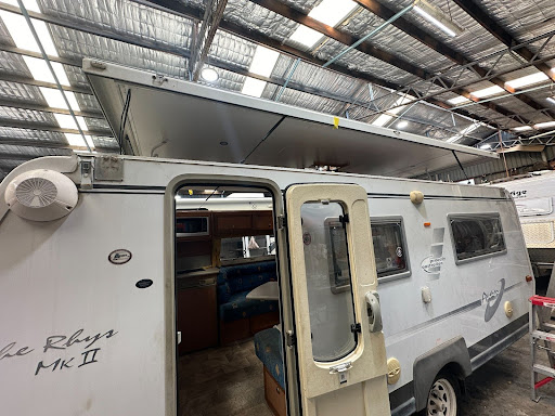 Caravan with damaged pop-top roof undergoing repairs in a workshop