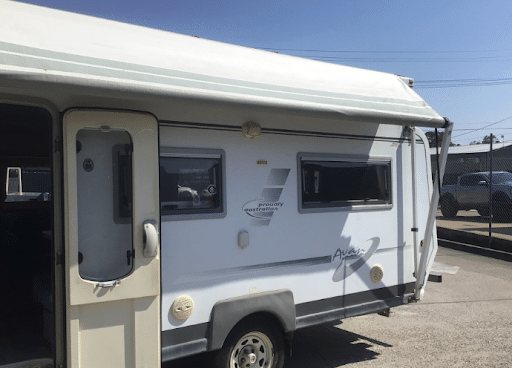 Caravan with damaged pop-top roof parked outside a repair shop, awaiting repairs