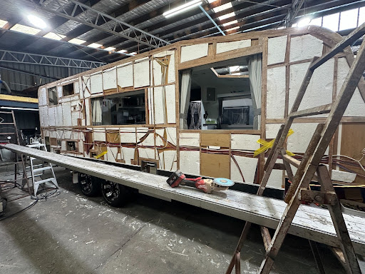 Caravan with dents in siding and roof prepped for repairs in a workshop