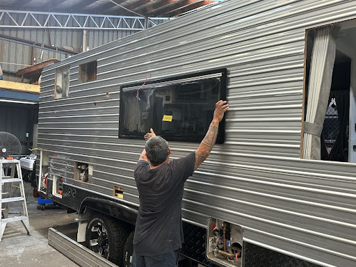 Caravan with dents in siding and a broken window requires repairs at a workshop