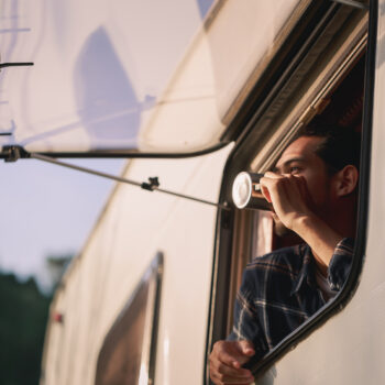 a man admires the view from his caravan window while he drinks a cup of tea