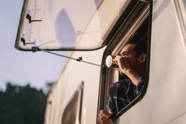 a man admires the view from his caravan window while he drinks a cup of tea