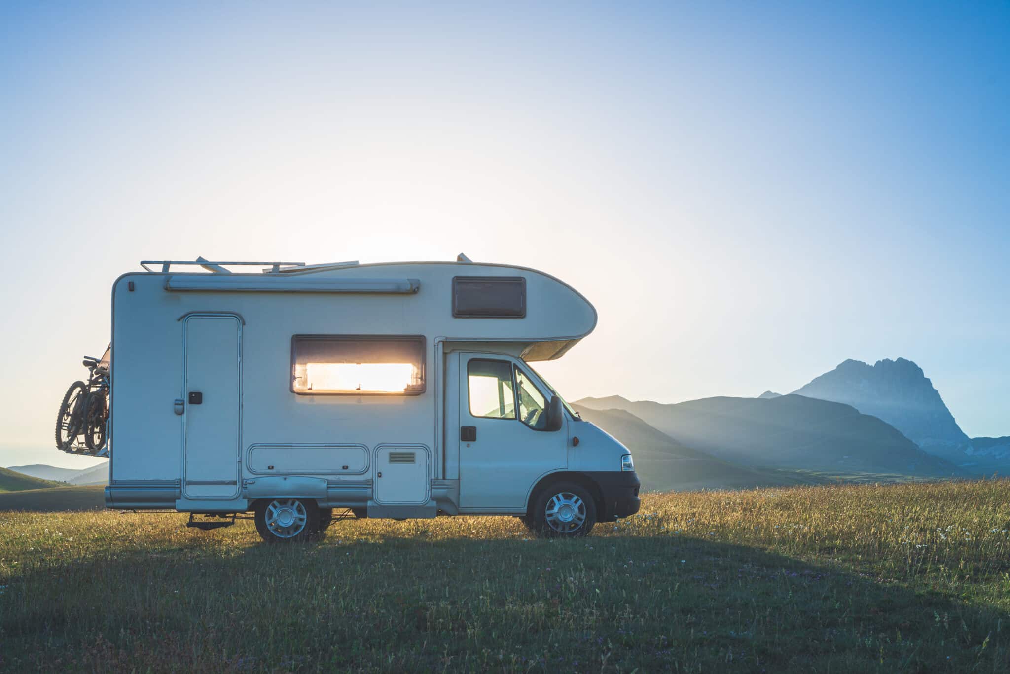 Sunset dramatic sky over camper van in Campo Imperatore highlands, Abruzzo, Italy. Epic clouds above unique highlands and rocky mountains landscape, alternative vanlife vacation concept.